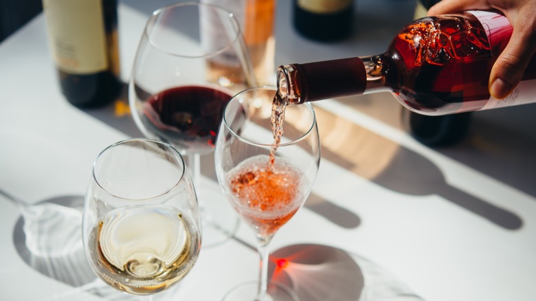 Hand pouring glass of wine into one of three glasses at a table.