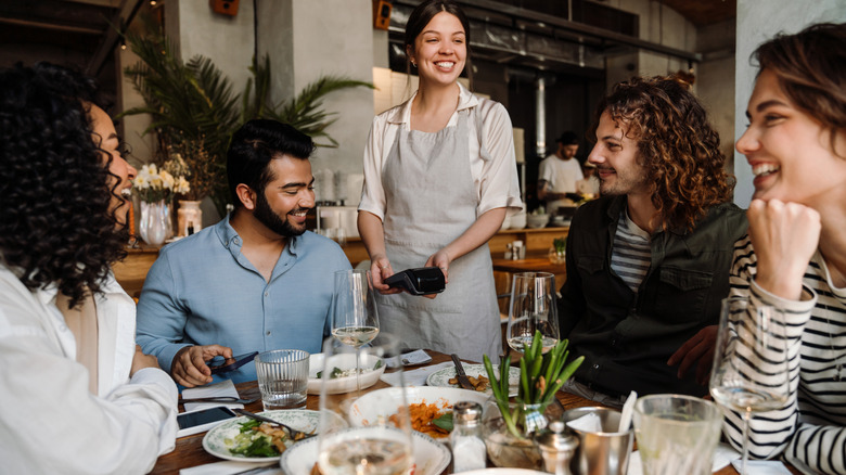 Man at a restaurant table with three friends paying bill with his phone