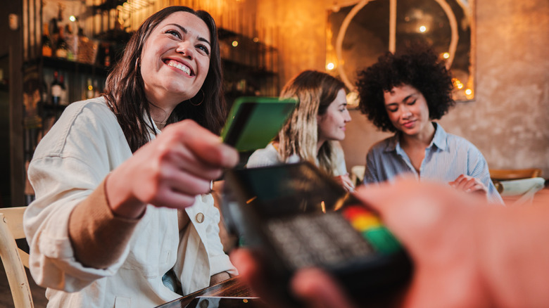 Woman at restaurant with two friends giving credit card to pay