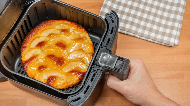 Hand holding air fryer basket with apple tart inside