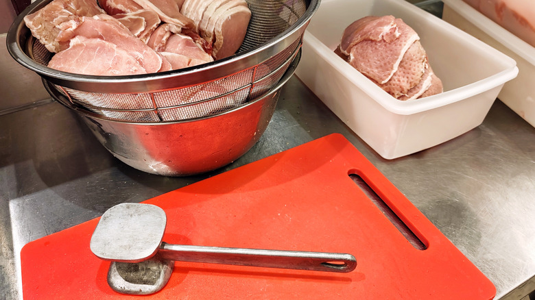 A meat tenderizer on a cutting board with meat in a bowl