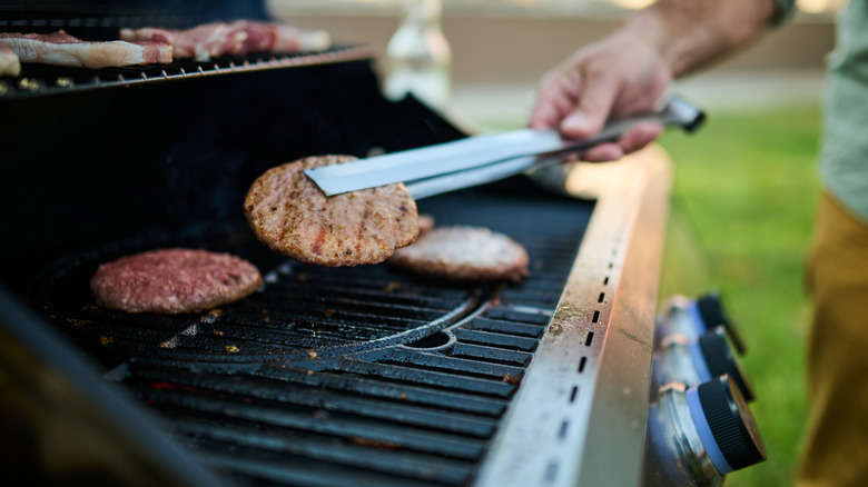 A man uses tongs to flip a burger on a grill