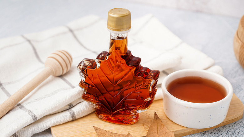 Maple syrup bottle on table atop a cutting board near napkins and a honey wand