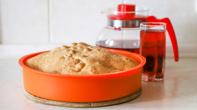 A pie in an orange silicon pan, with a coffee pot and glass behind it