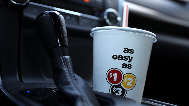 A McDonald's cup in a car cupholder near the gear shift, displaying the "as easy as $1 $2 $3" value menu slogan