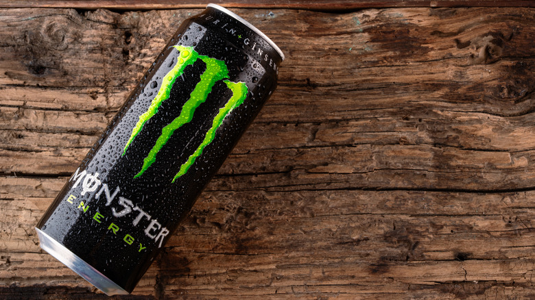A can of Monster Energy on a wood table with beads of moisture clinging to the side.