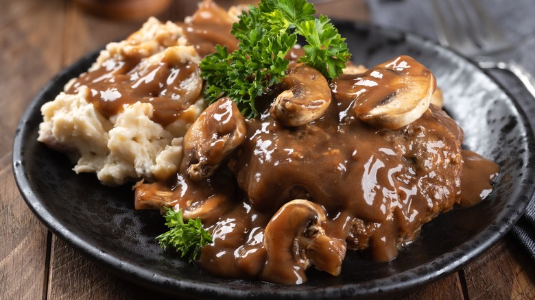 A plate of Salisbury steak coated in mushroom gravy, served with broccoli and mashed potatoes.