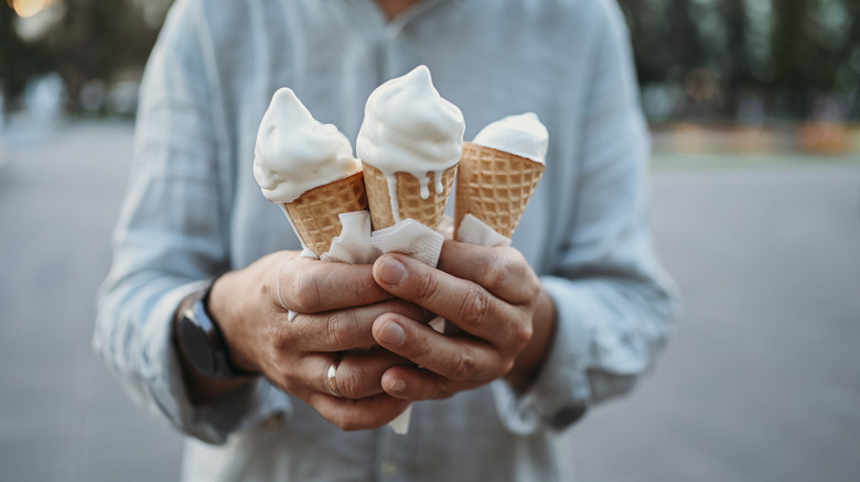 A man holding three melting vanilla ice cream cones.