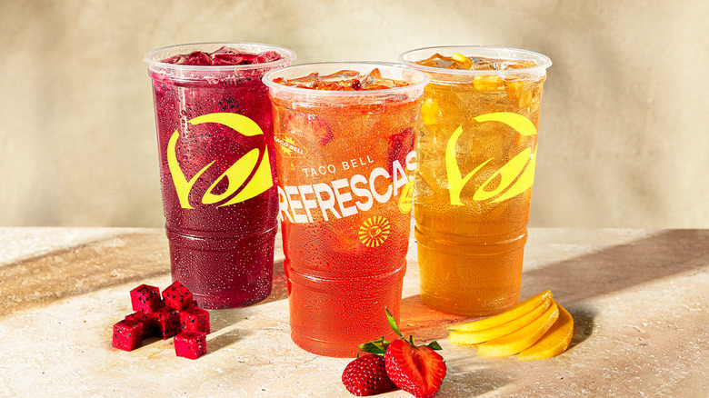 A trio of Taco Bell Agua Refrescas with fruit against a neutral background
