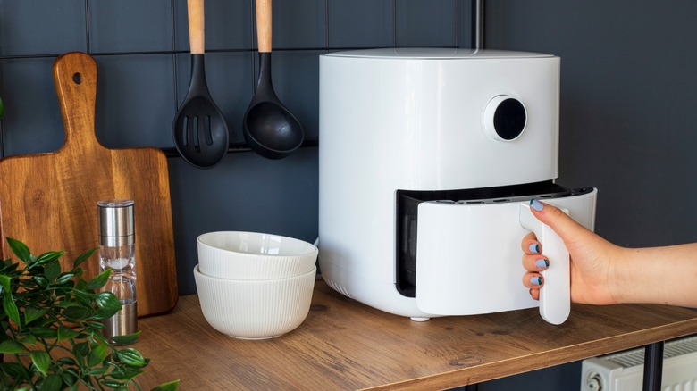 A woman opens a white air fryer on a wooden table