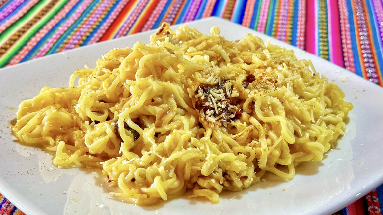 Homemade instant ramen carbonara on a white plate atop a colorful tablecloth