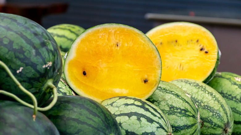 A yellow watermelon, sliced open, alongside other watermelons