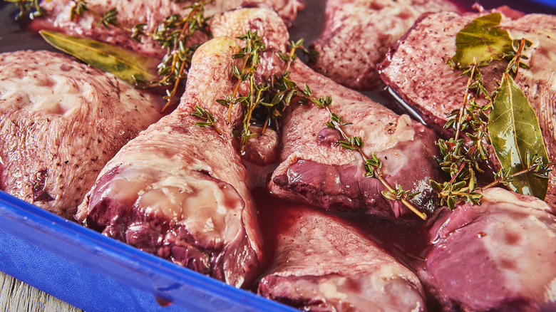 Chicken thighs marinating with fresh herbs in a blue tray.
