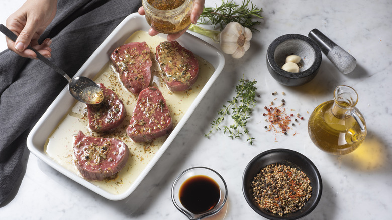 Raw slabs of beef being coated in sauce and seasonings in a white dish