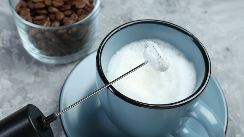 A milk frothing wand in a mug of frothed milk