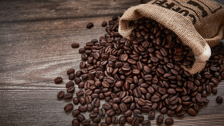 Coffee beans spilling from a burlap bag onto a wooden surface.