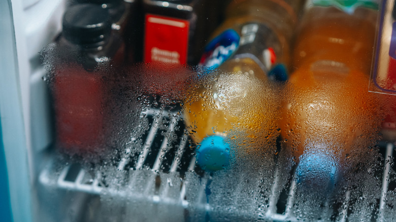 A refrigerator door with soda and juice bottles covered in condensation