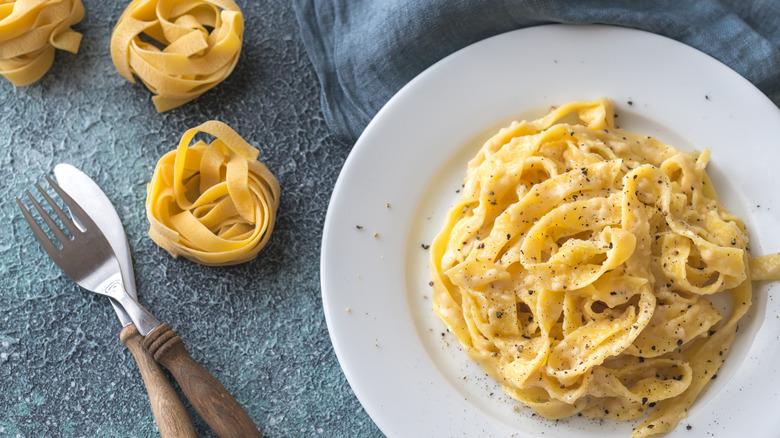 Fettuccine Alfredo with cheese and pepper on a white plate.
