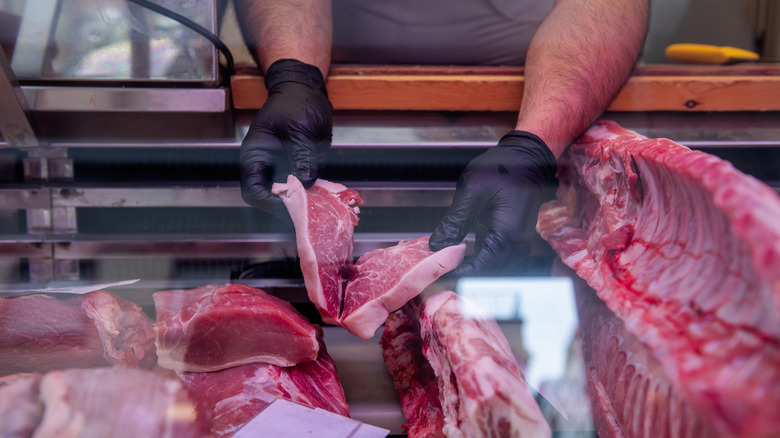 Hands arranging meat in a butcher's shop