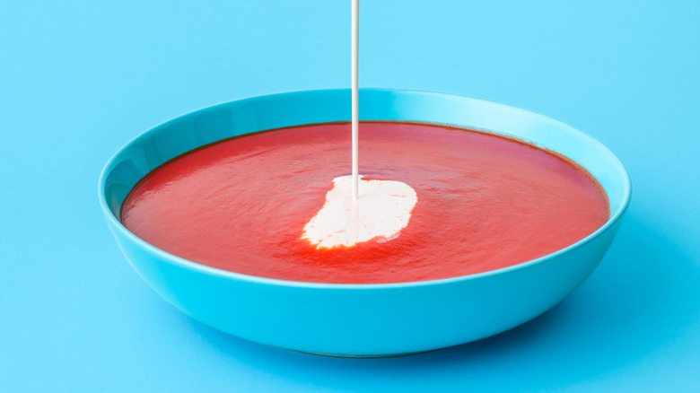 cream being poured into tomato soup in blue bowl