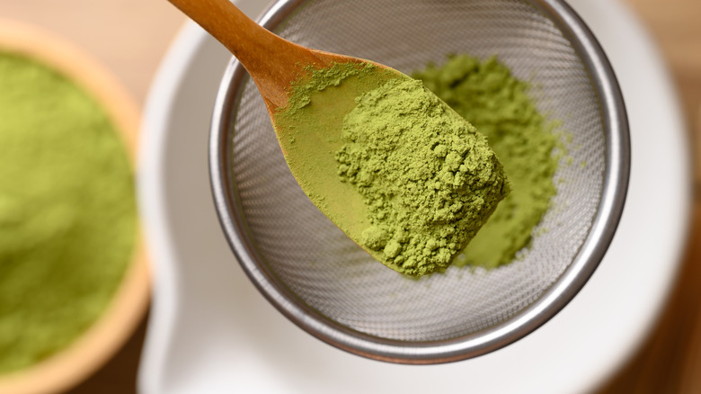 Wooden spoon of matcha powder over a small metal sieve