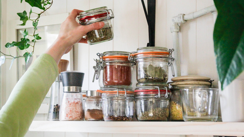 hand placing a glass jar of spices on a shelf with other spice jars