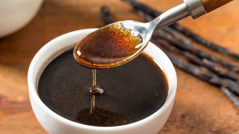 A spoonful of vanilla extract being measured out from a small white bowl