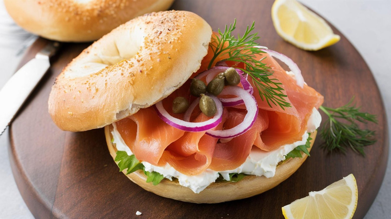 A bagel with lox, capers, red onions, and dill on a wooden board