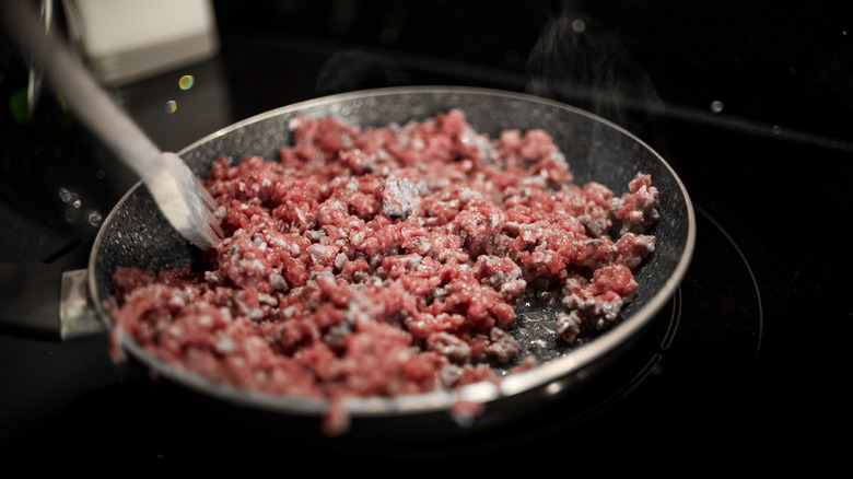 A person cooking ground beef in a pan.