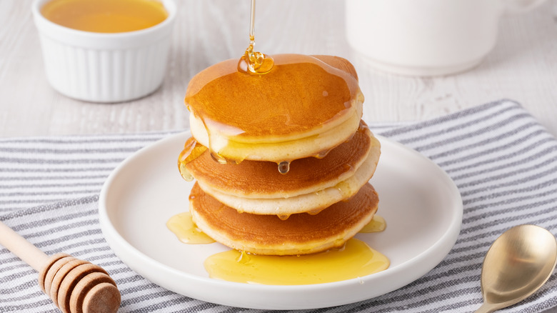 Delicious three-tiered fluffy pancakes with syrup served on a white plate for breakfast.