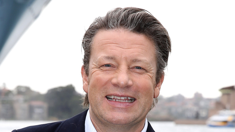 Jamie Oliver smiling in a black suit jacket at the waterfront