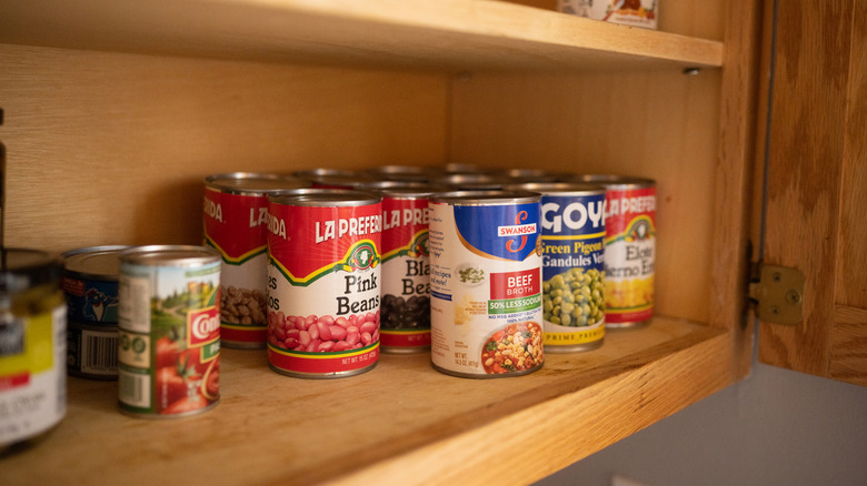 Cans of beans and soup line a pantry shelf