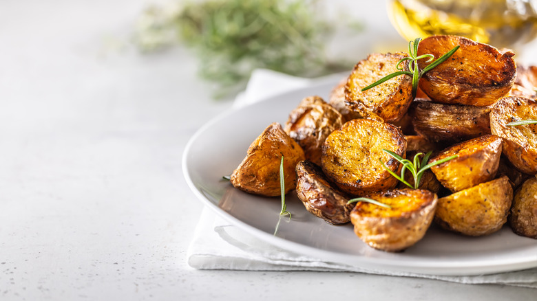 Golden baked potatoes on a white plate with rosemary