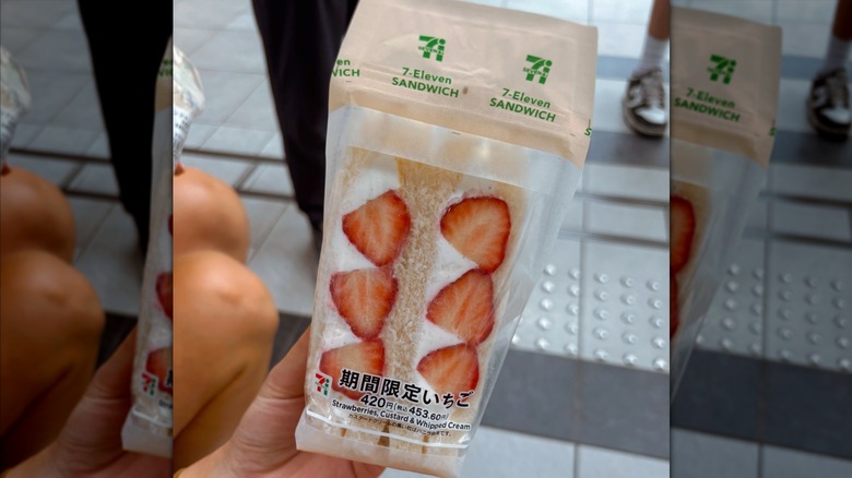 A hand holding a packaged strawberries and cream sandwich from 7-Eleven Japan