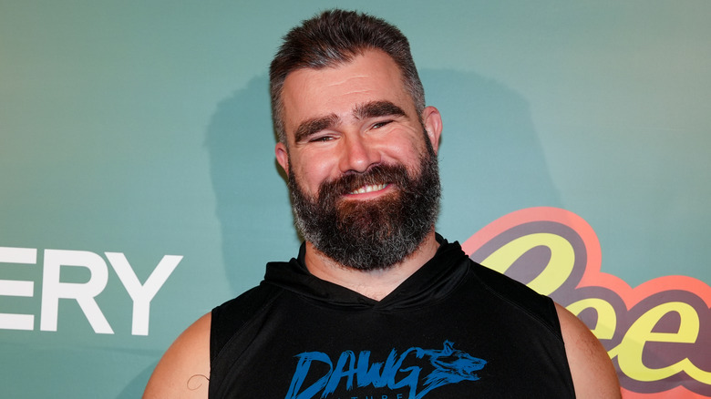 Smiling Jason Kelce wearing a black, sleeveless top in front of a light green background