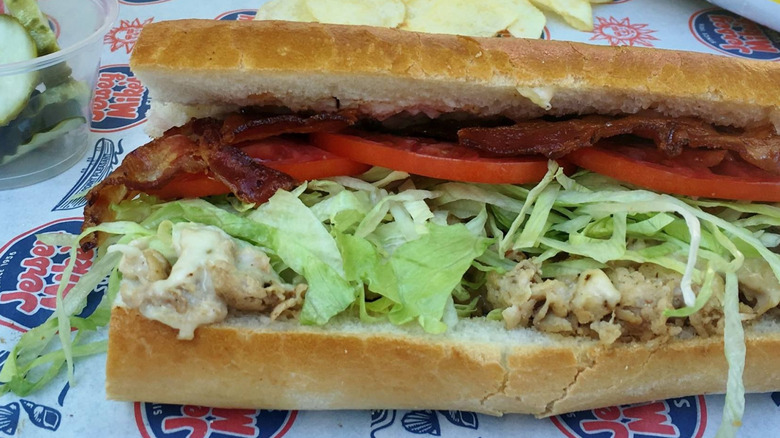 An open Jersey Mike's sub with chicken salad, bacon, lettuce, and sliced tomato