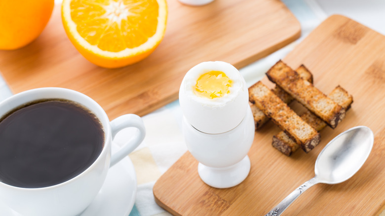 Boiled eggs for breakfast with coffee, oranges, and toast served on wooden boards.