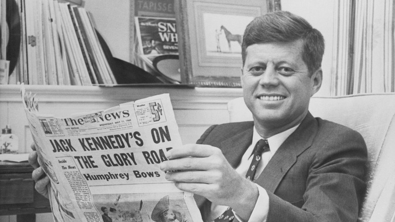 John F. Kennedy photographed relaxing in his home holding a newspaper reporting his smashing victory over Senator Humphrey in the West Virginia Primary.