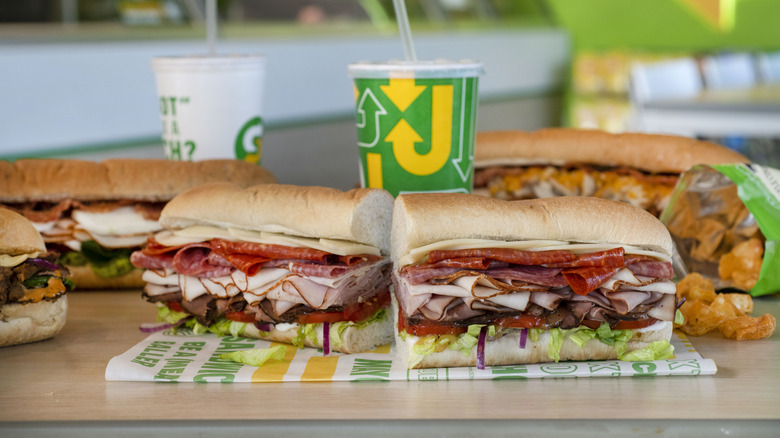 Subway sandwiches displayed on counter with drinks and open bag of chips.
