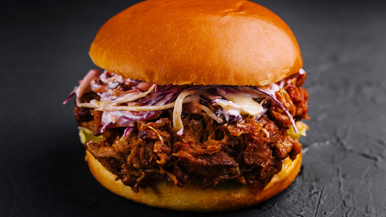 A pulled pork sandwich on a bun topped with thick coleslaw with a dark background.