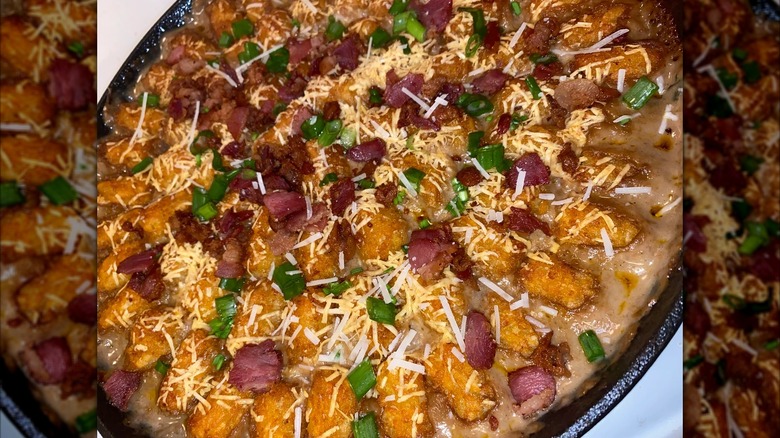 A cowboy casserole with tater tots, bacon bits, and green olives on top in a large black dish