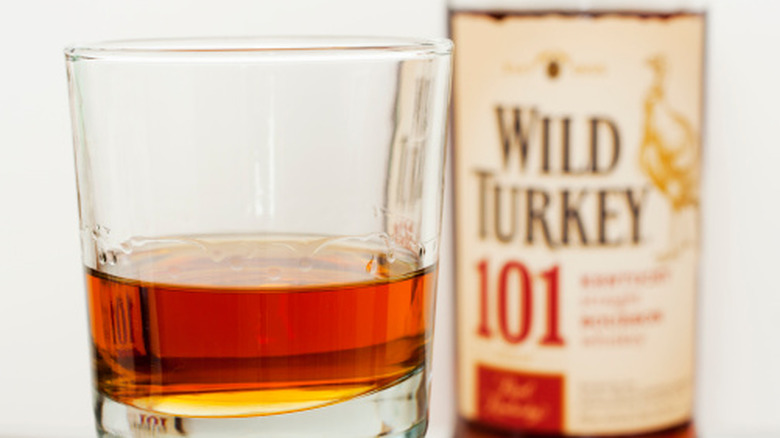 A bottle of Wild Turkey in the background and a short tumbler of the bourbon in the forground
