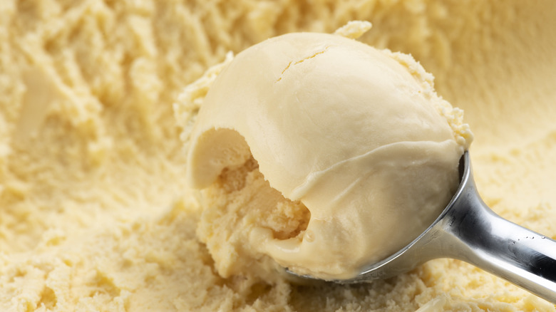 An ice cream scooper picking up a ball of vanilla ice cream