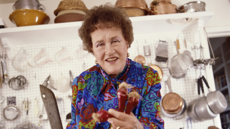 Julia Child stands before a wall of kitchen tools