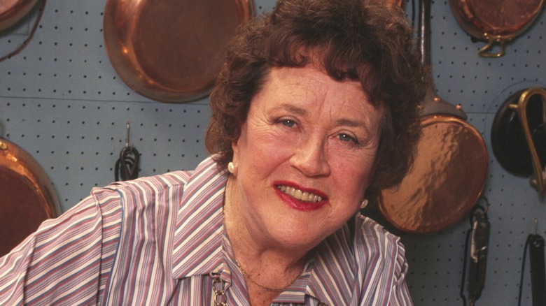 Julia Child smiling in a kitchen in front of copper pots and pans.
