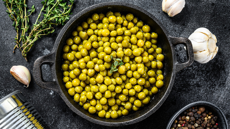 Canned peas in small black frying pan alongside garlic, thyme, and black pepper