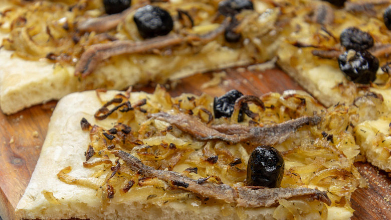 Slices of French-style pissaladière on a wood cutting board.
