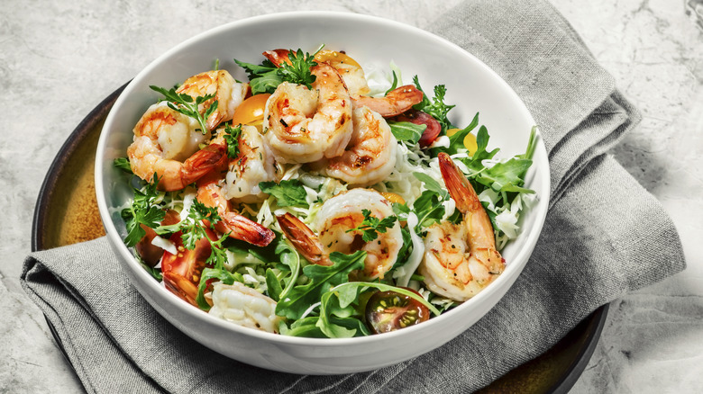 A shrimp salad in a bowl on a grey cloth on a tray.