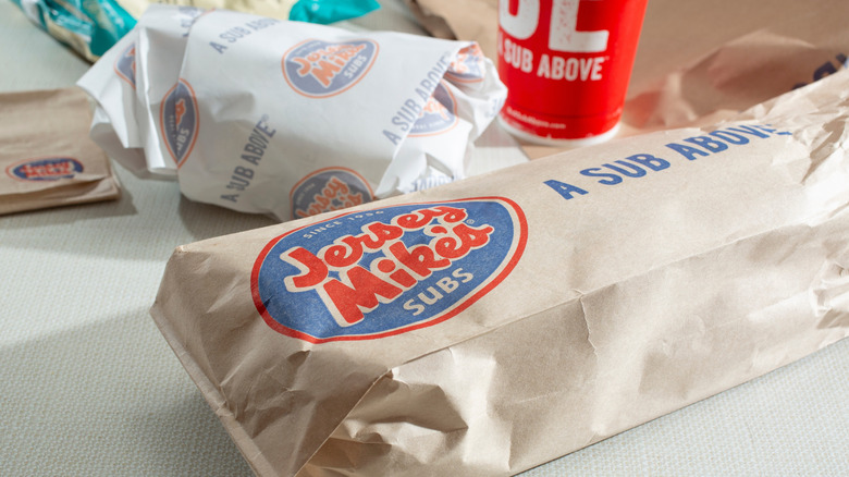 A Jersey Mike's sandwich bag near a wrapped sandwich and red fountain drink cup