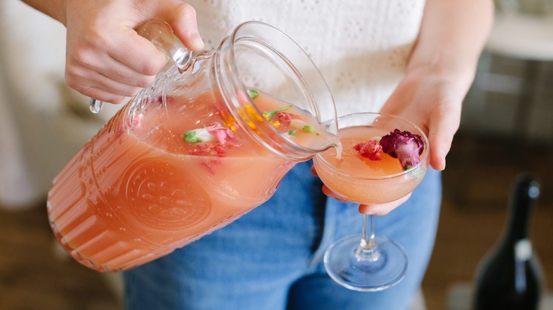 A person pouring a cocktail out of a large pitcher into a margarita glass